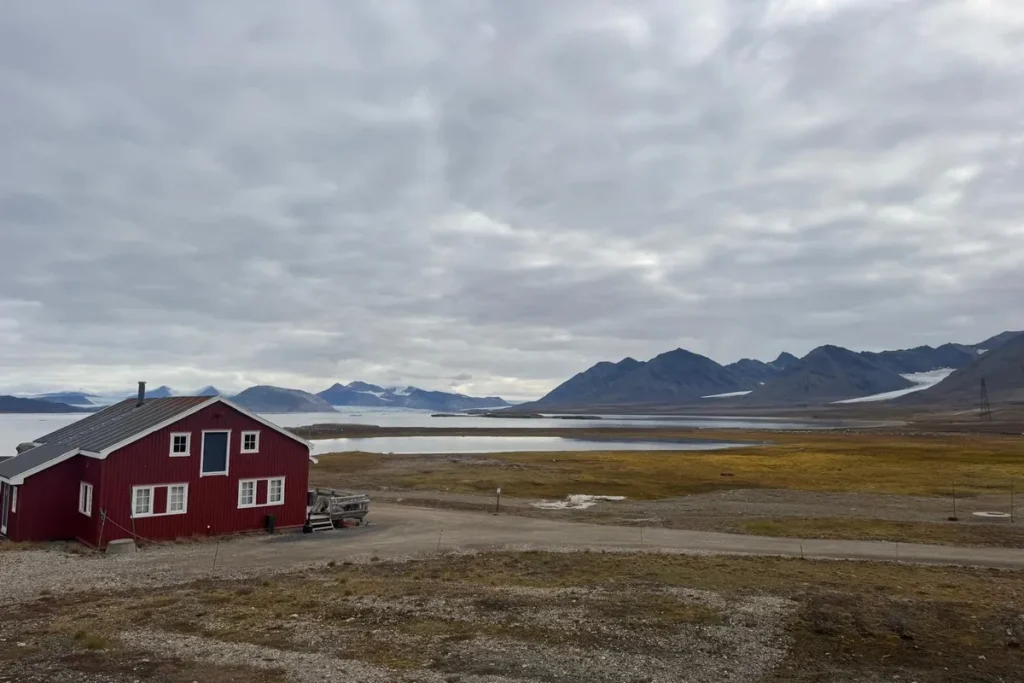Czerwony domek nad fiordem na Svalbardzie – widok na góry i lodowce w tle