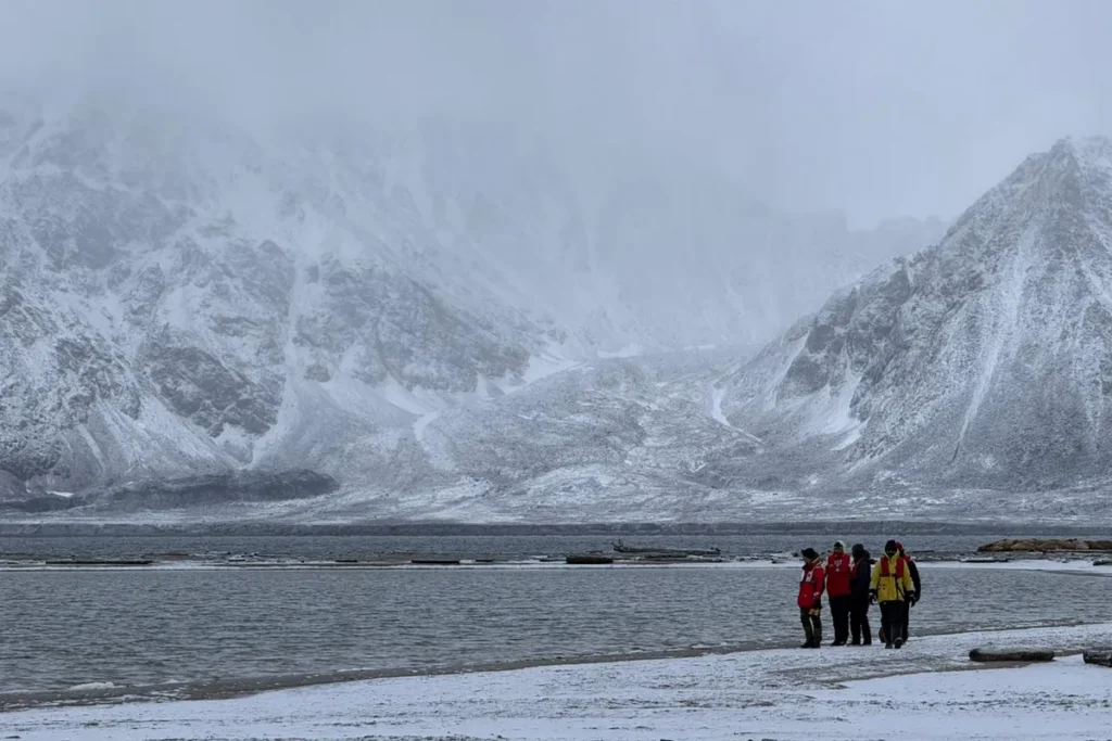 Grupa ludzi w czerwonych kurtkach idzie wzdłuż zaśnieżonego brzegu podczas rejsu na Svalbard
