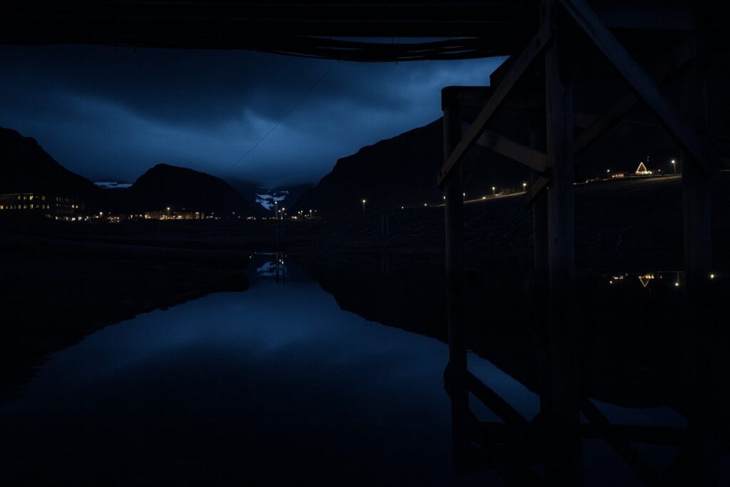 Longyearbyen nocą z odbiciem świateł w wodzie i górami w tle